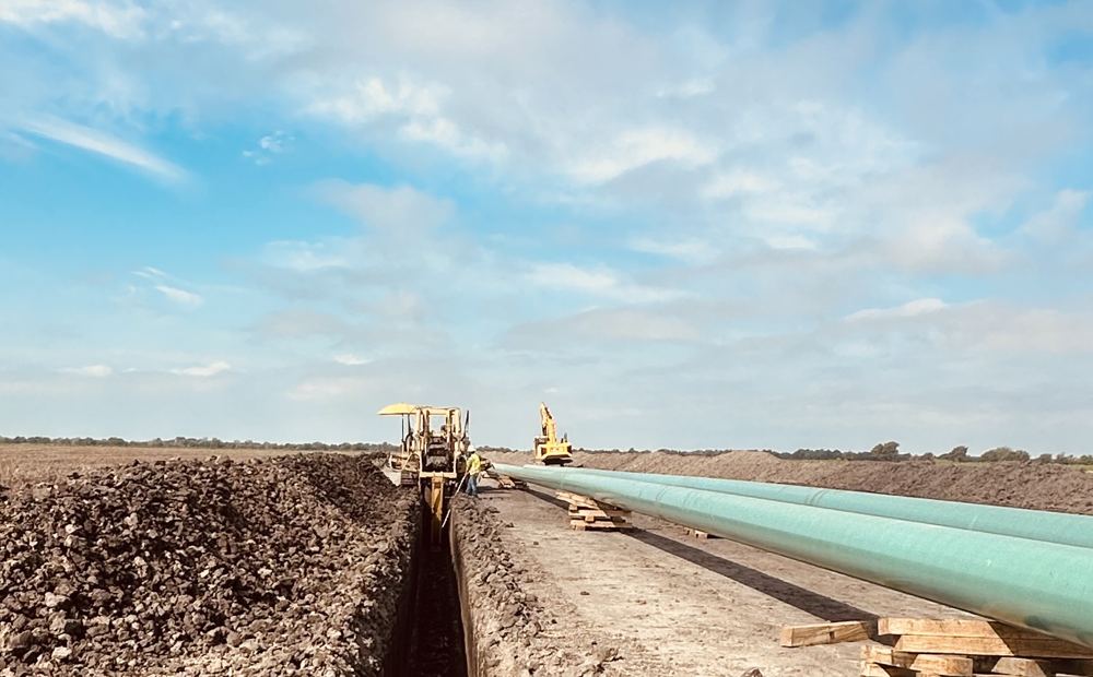 Trencher cutting a pipeline ditch beside strung pipe